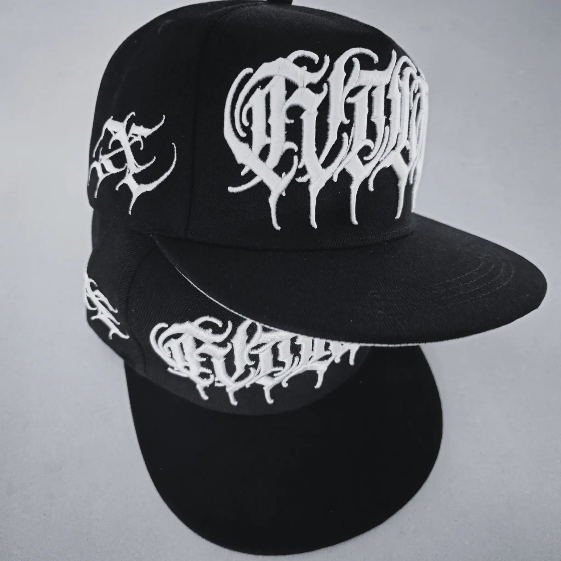 A black snapback cap with white 3D embroidered lettering and an artist signature logo on the side. RTLA-Apparel
