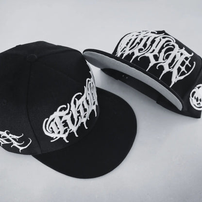 A black snapback cap with white 3D embroidered lettering and an artist signature logo on the side. RTLA-Apparel