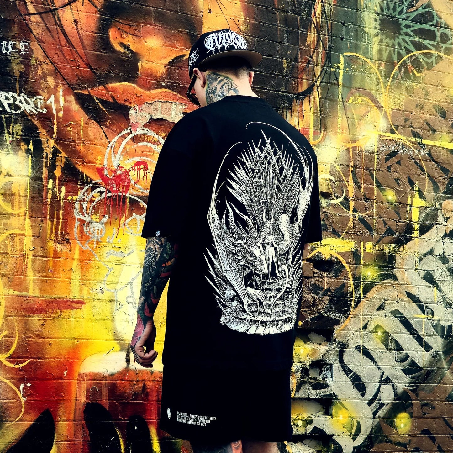Person wearing a black t-shirt with a dragon design in front of a graffiti-covered wall.