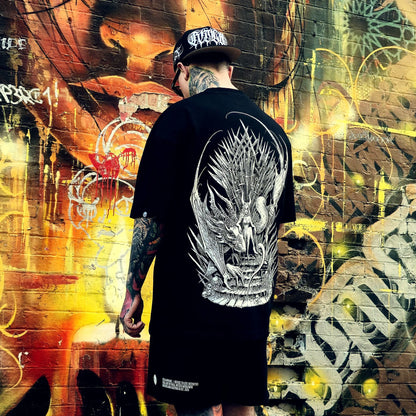 Person wearing a black t-shirt with a dragon design in front of a graffiti-covered wall.