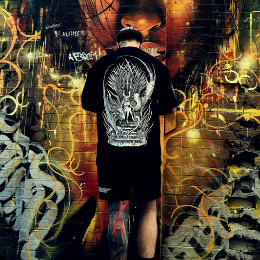 Person wearing a black t-shirt with a white graphic design against a colorful graffiti wall.