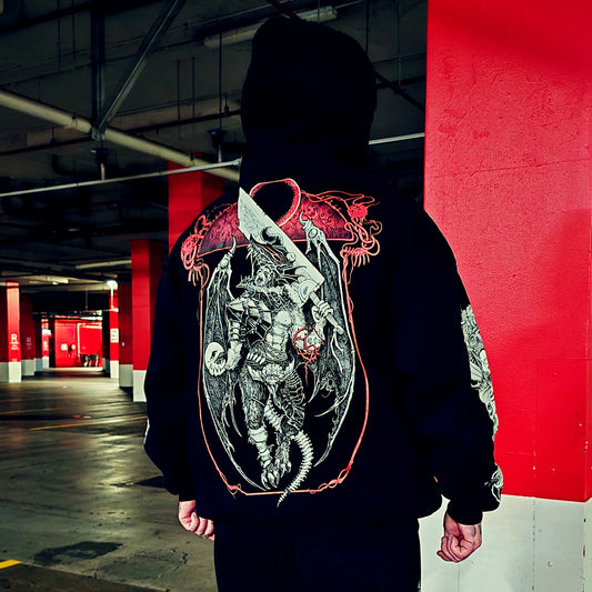 A person standing in a parking garage wearing a black hoodie from the back, which features a large, detailed graphic print of a winged knight holding a sword and shield, outlined in red.