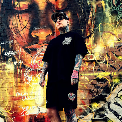 Person wearing a black t-shirt with a logo in front of a colorful graffiti wall.