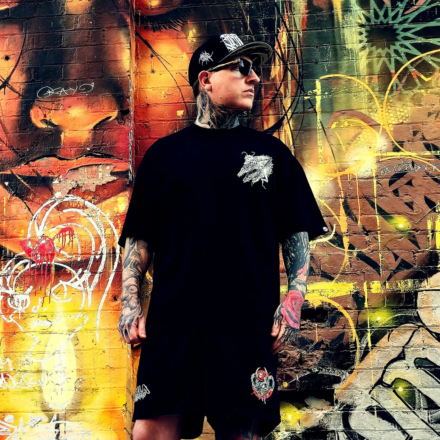 Person wearing a black t-shirt with a white logo in front of a colorful graffiti wall.