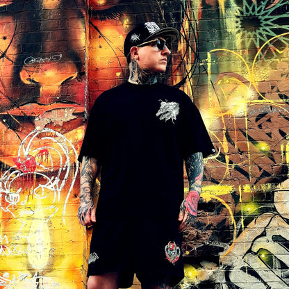 Person wearing a black t-shirt with a white logo in front of a colorful graffiti wall.