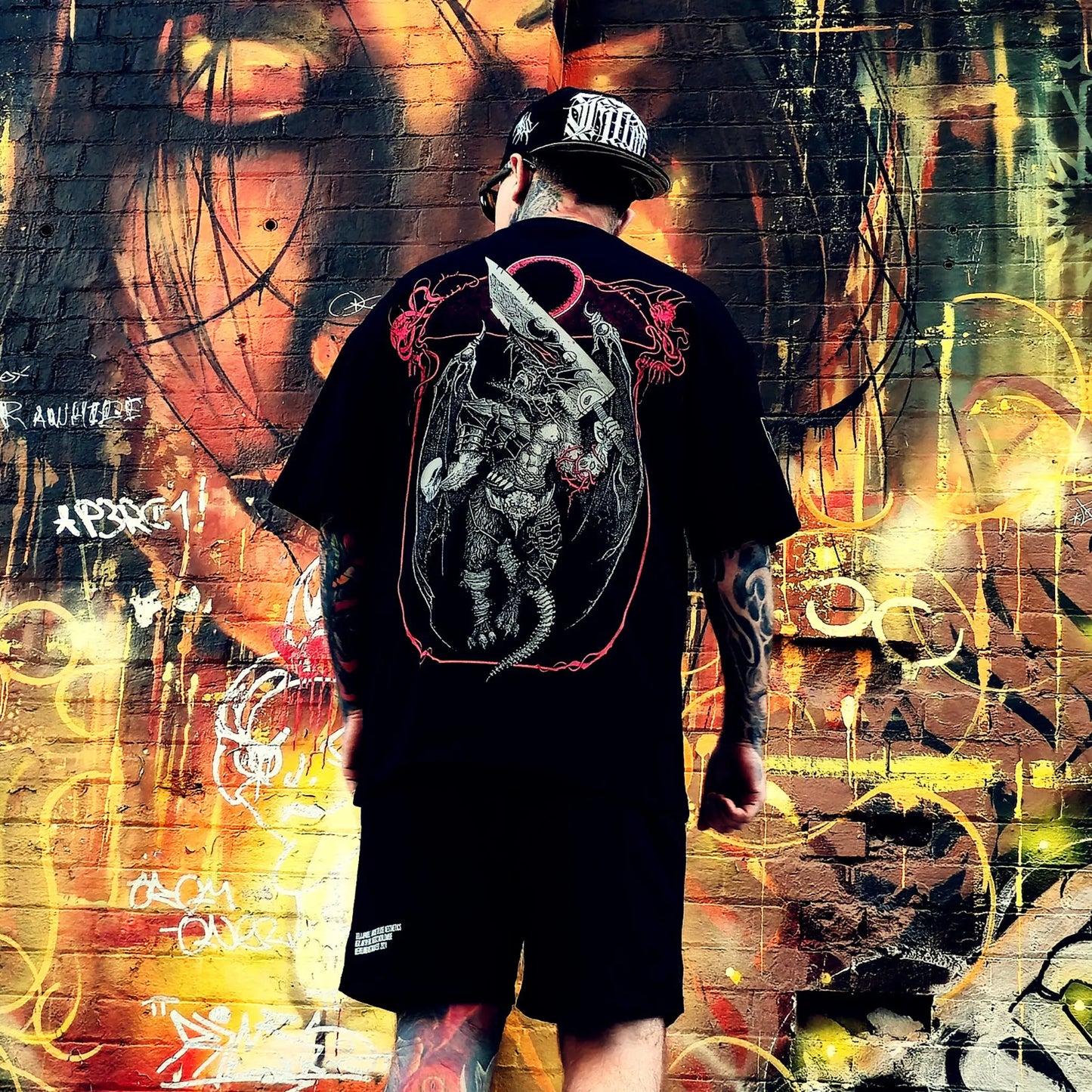 Person wearing a black t-shirt with a graphic design, standing in front of a colorful graffiti wall.