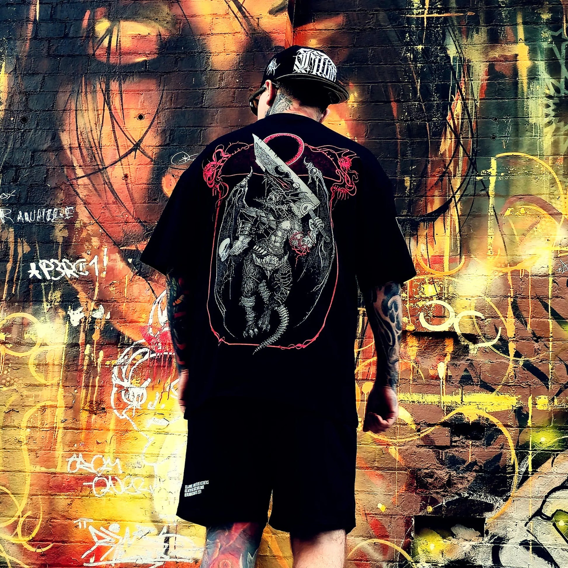 Person wearing a black t-shirt with a graphic design, standing in front of a colorful graffiti wall.