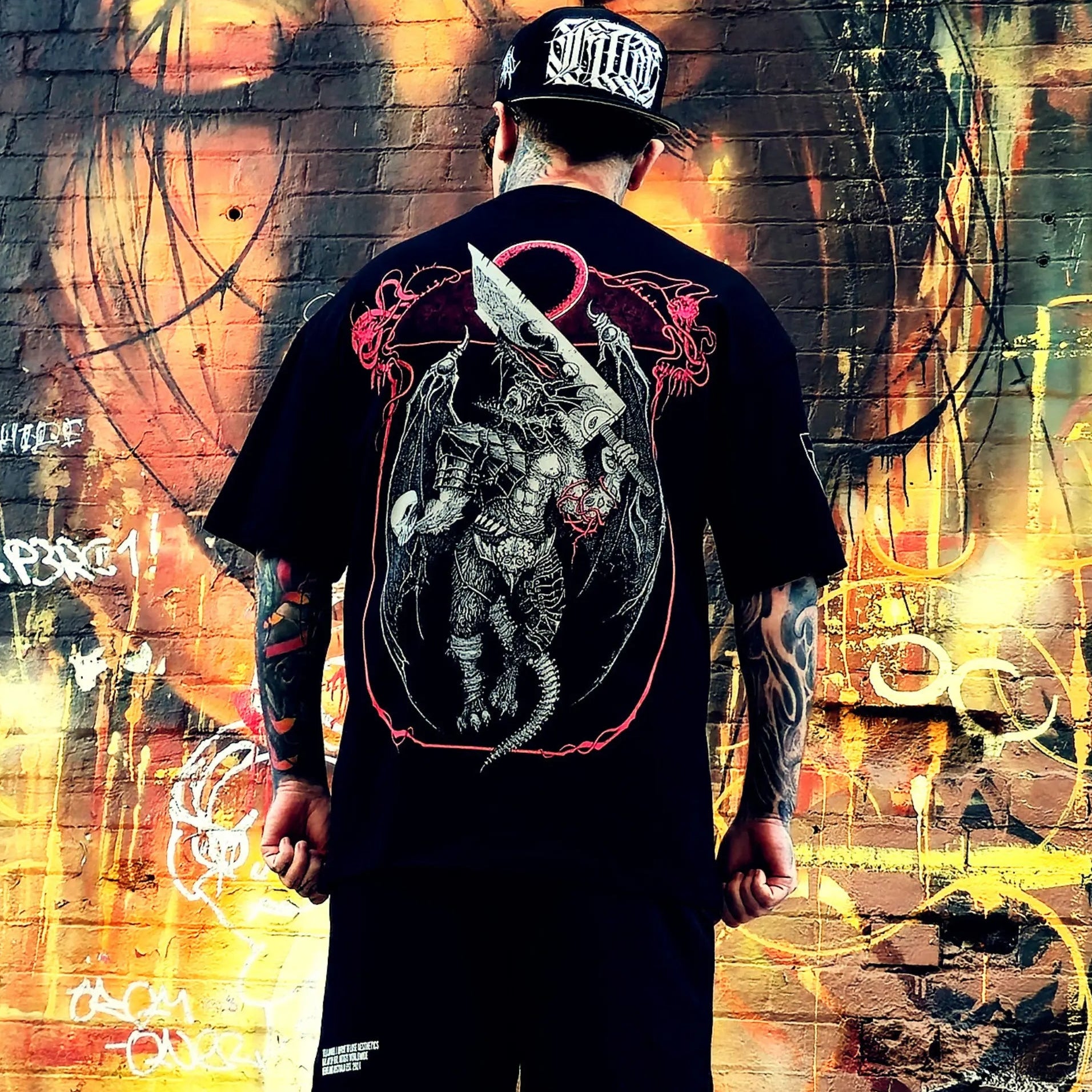 Person wearing a black t-shirt with a graphic design in front of a colorful graffiti wall.