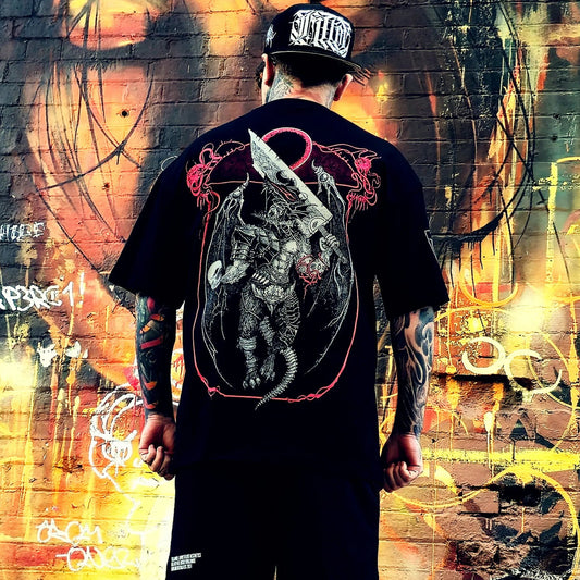 Person wearing a black t-shirt with a graphic design in front of a colorful graffiti wall.