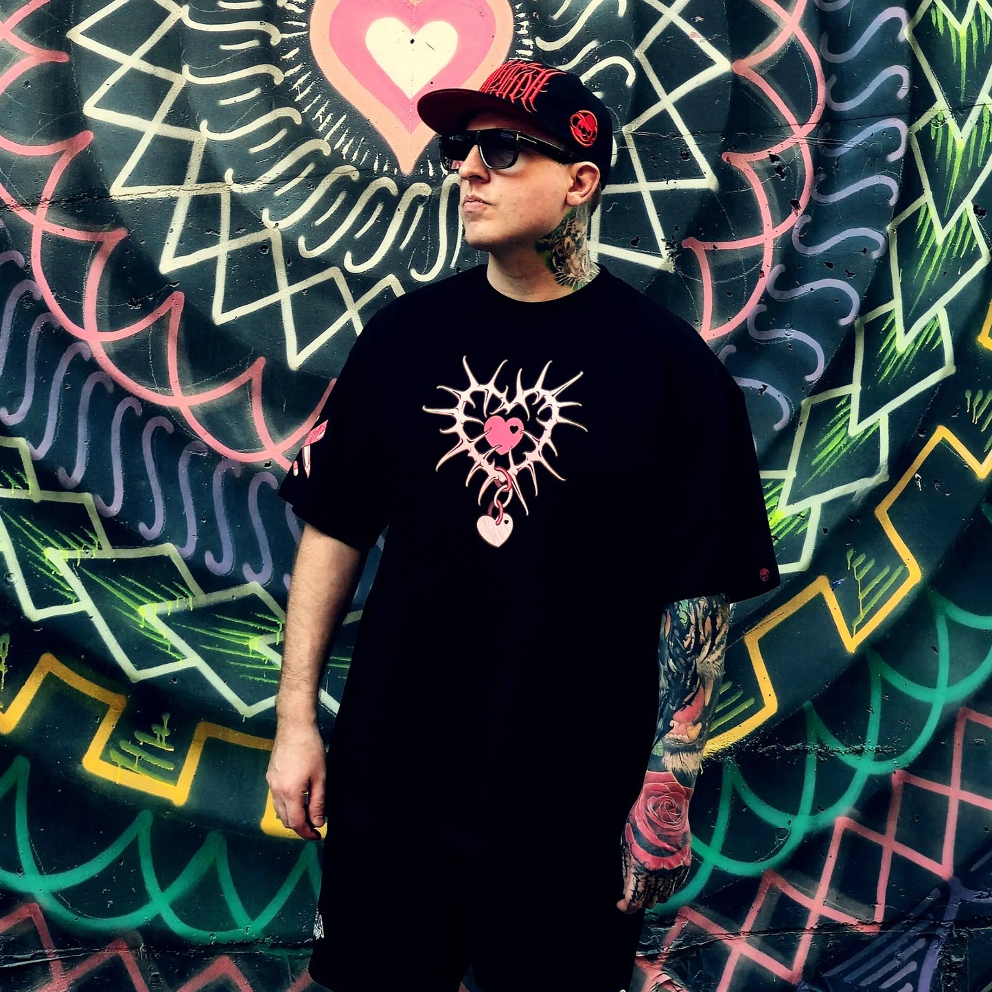 Person wearing a black t-shirt with a unique design in front of a colorful mural.