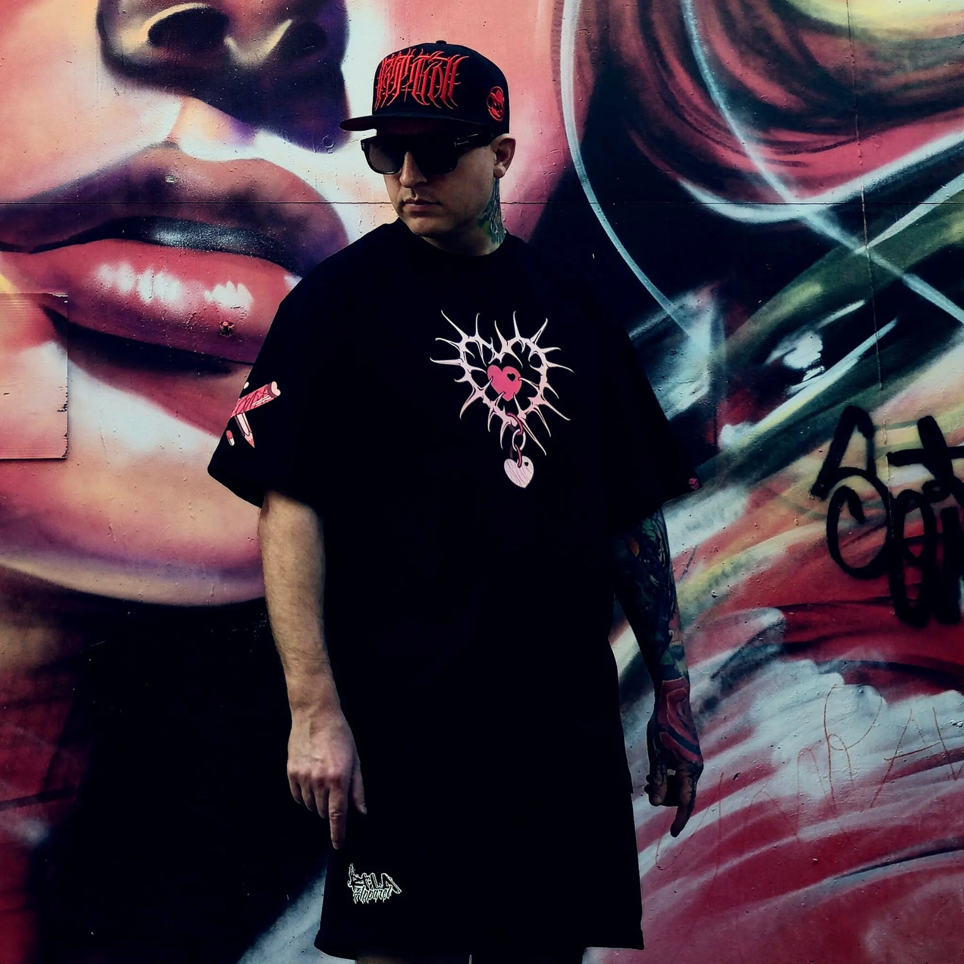 Person wearing a black t-shirt with a graphic design in front of a colorful mural.