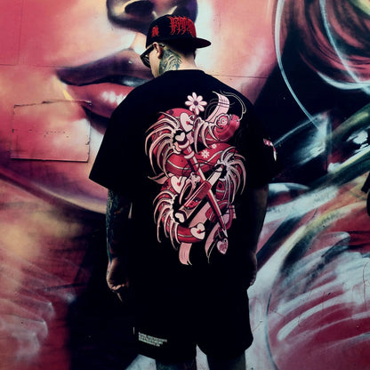 Person wearing a black t-shirt with a red and white graphic design, standing in front of a graffiti wall.