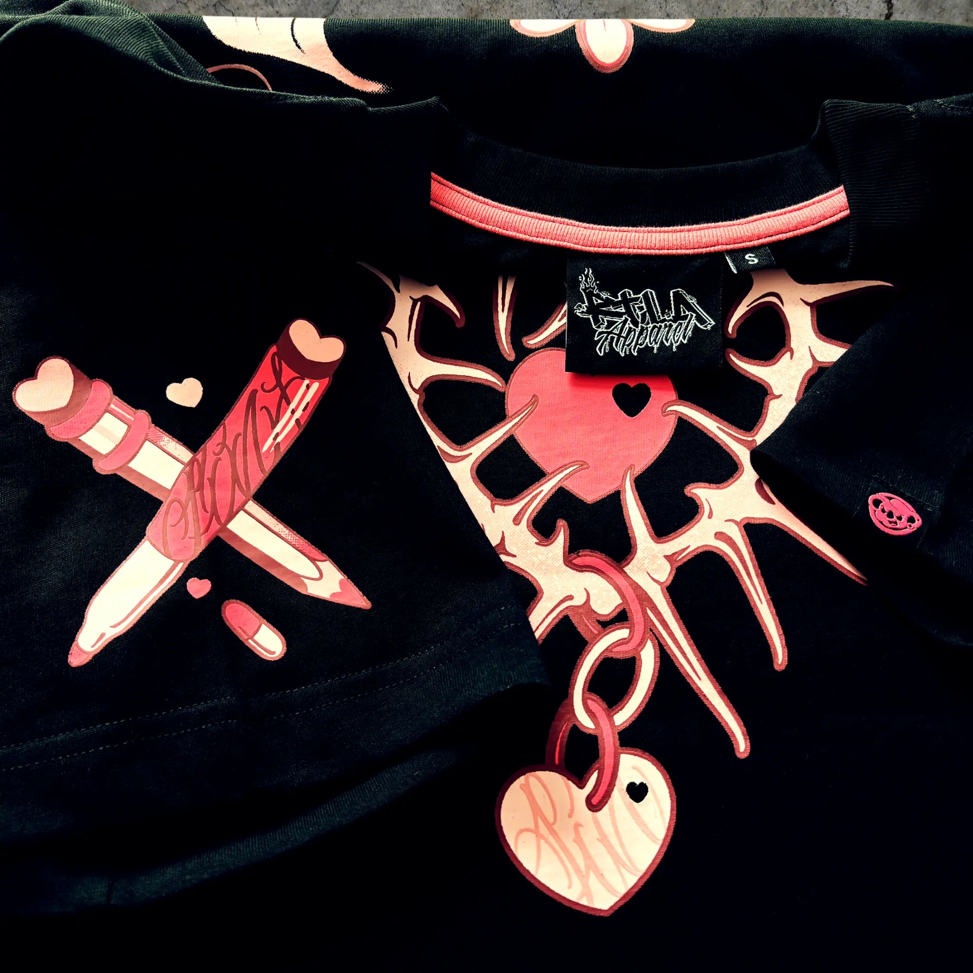Black shirt with pink skeleton design and heart shapes on a dark background