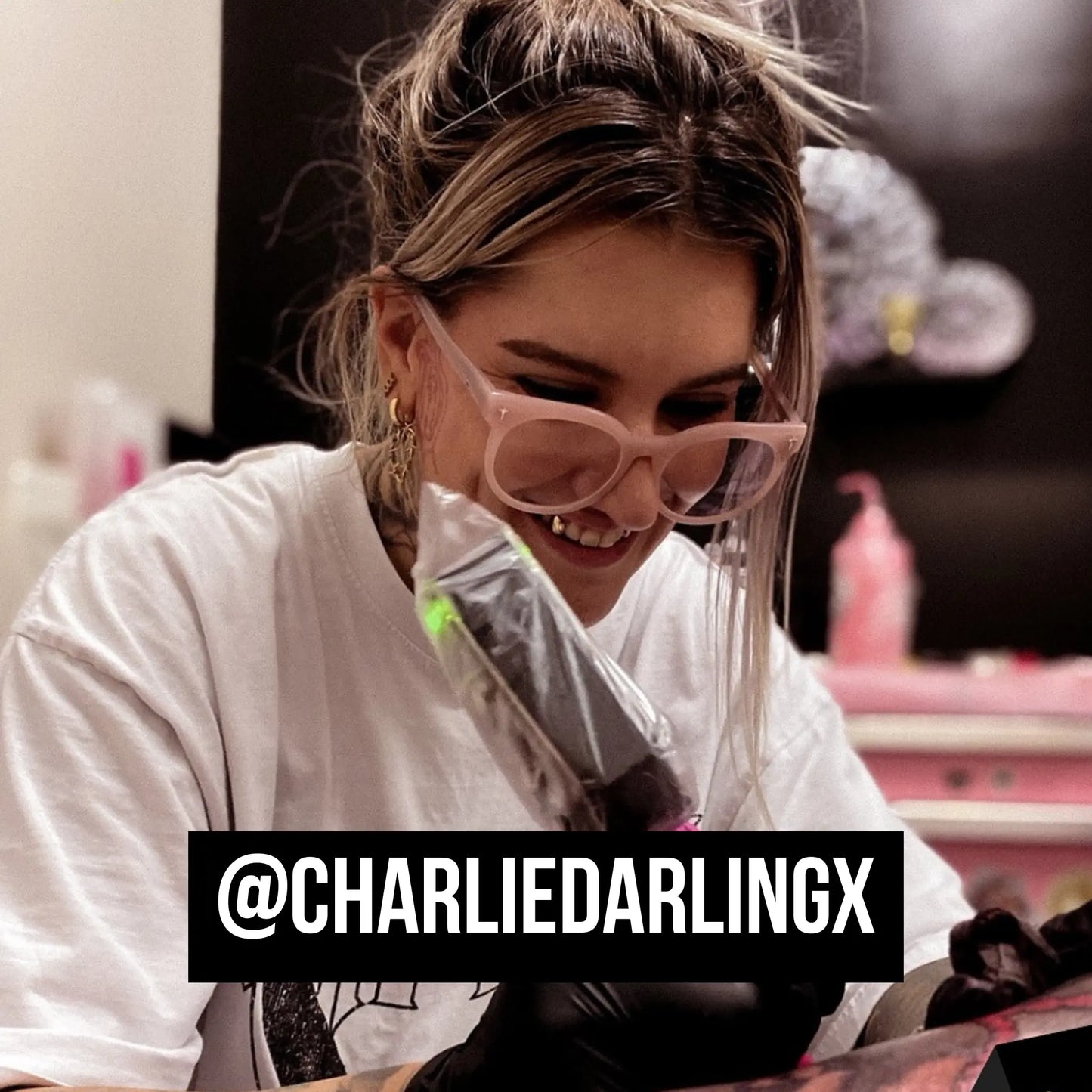 @charliedarlingx wearing pink sunglasses and a white shirt with a blurred background