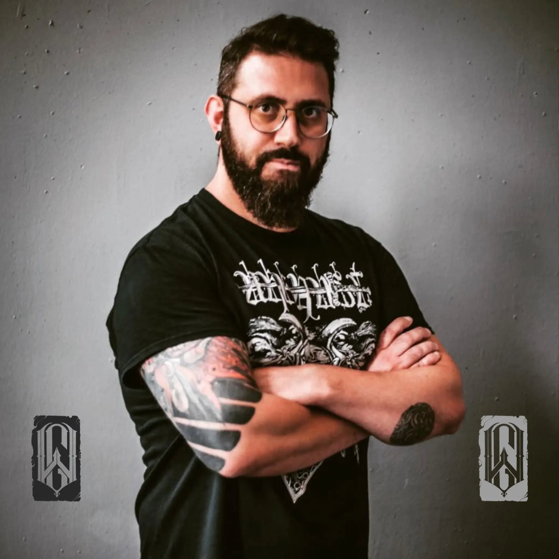 Man with tattoos and a beard wearing a black t-shirt with graphic designs against a gray background