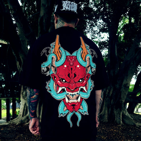 Person wearing a black t-shirt with a colorful demon design in a forest setting