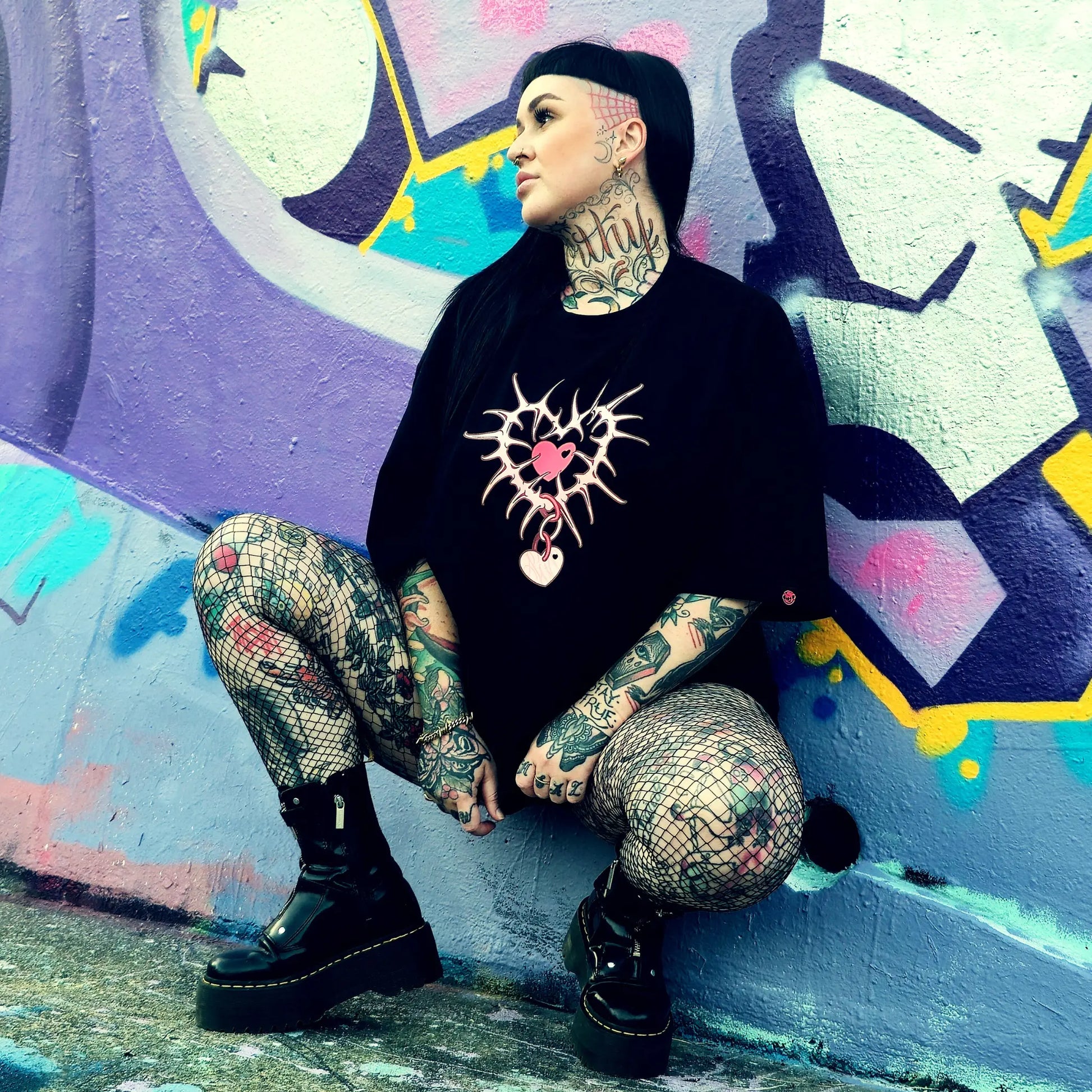 Person with tattoos sitting against a colorful graffiti wall