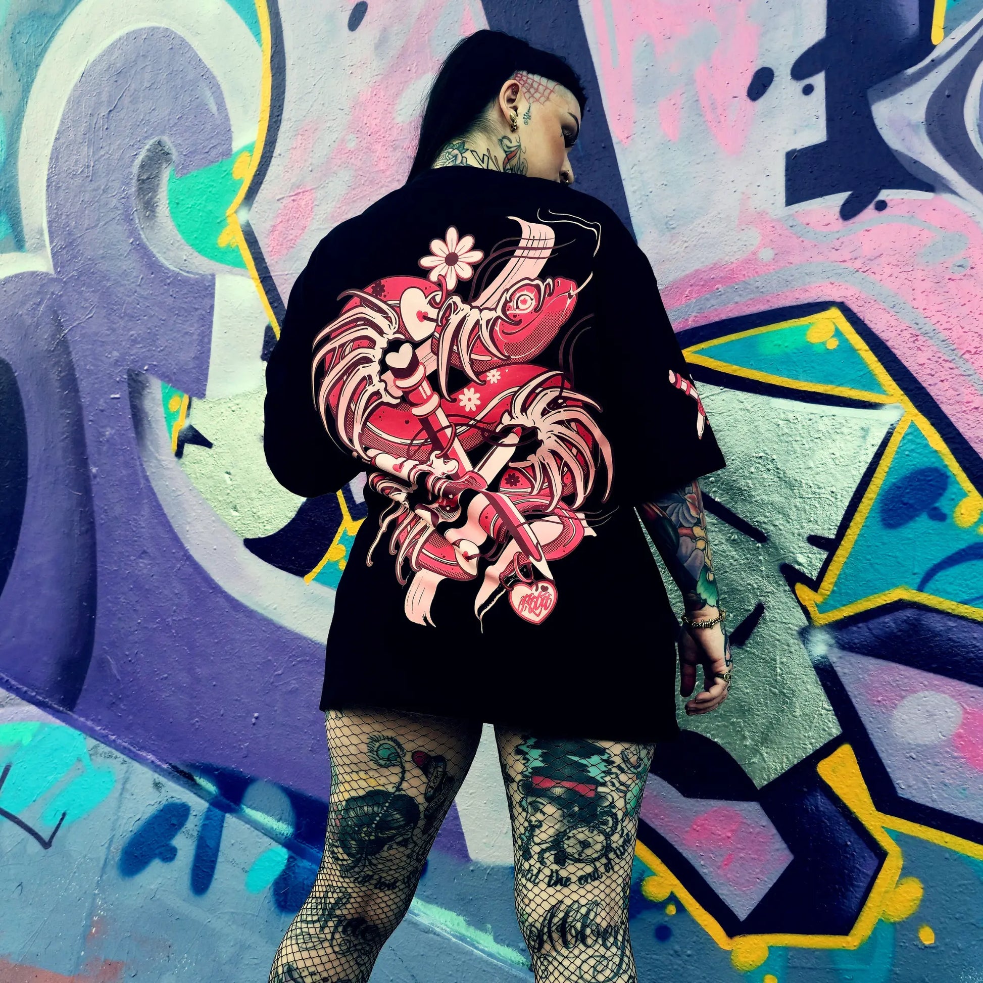 Person wearing a black hoodie with a red and pink floral design against a colorful graffiti wall.
