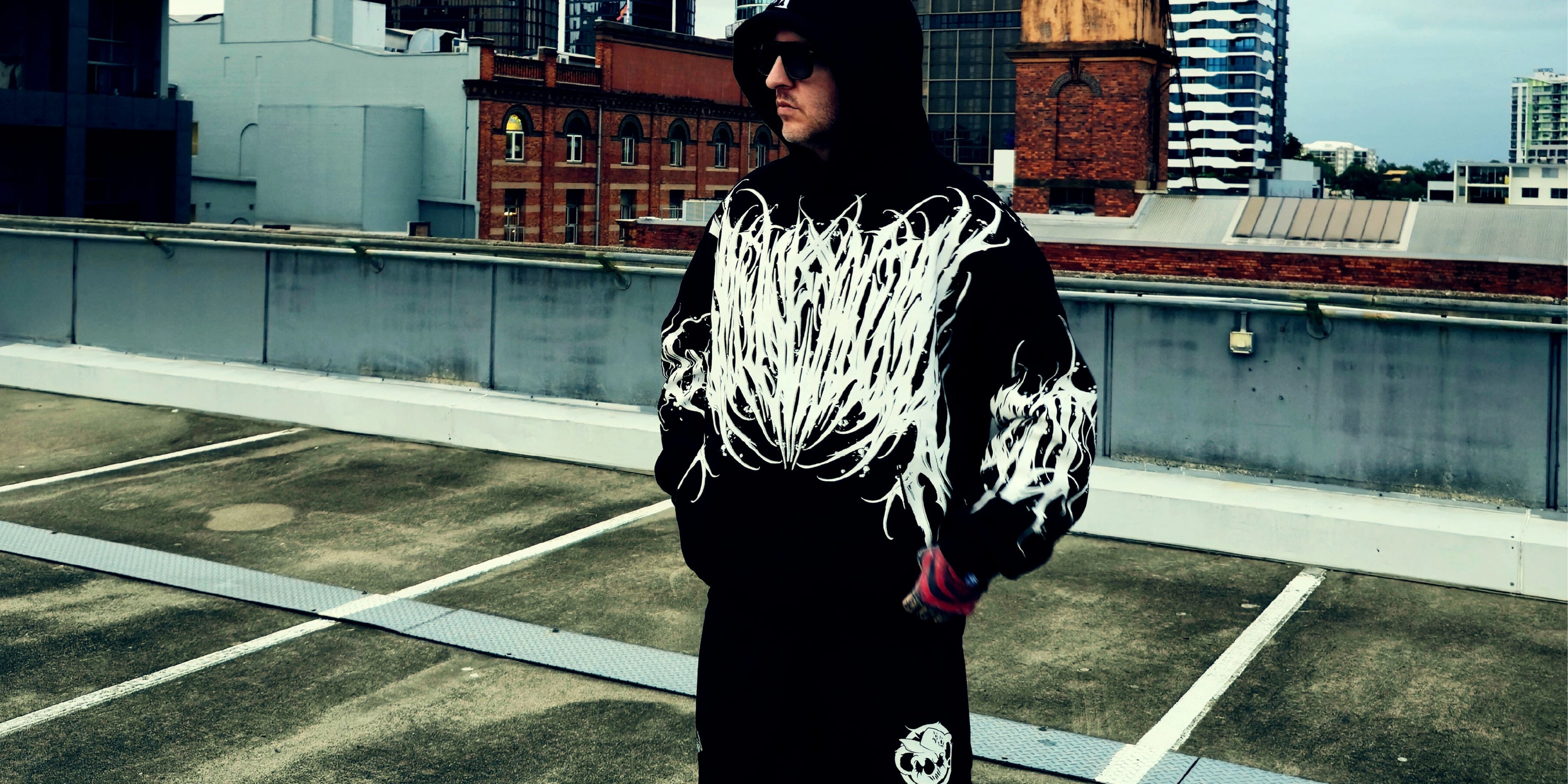 Person wearing a black hoodie with white designs on a rooftop with urban buildings in the background