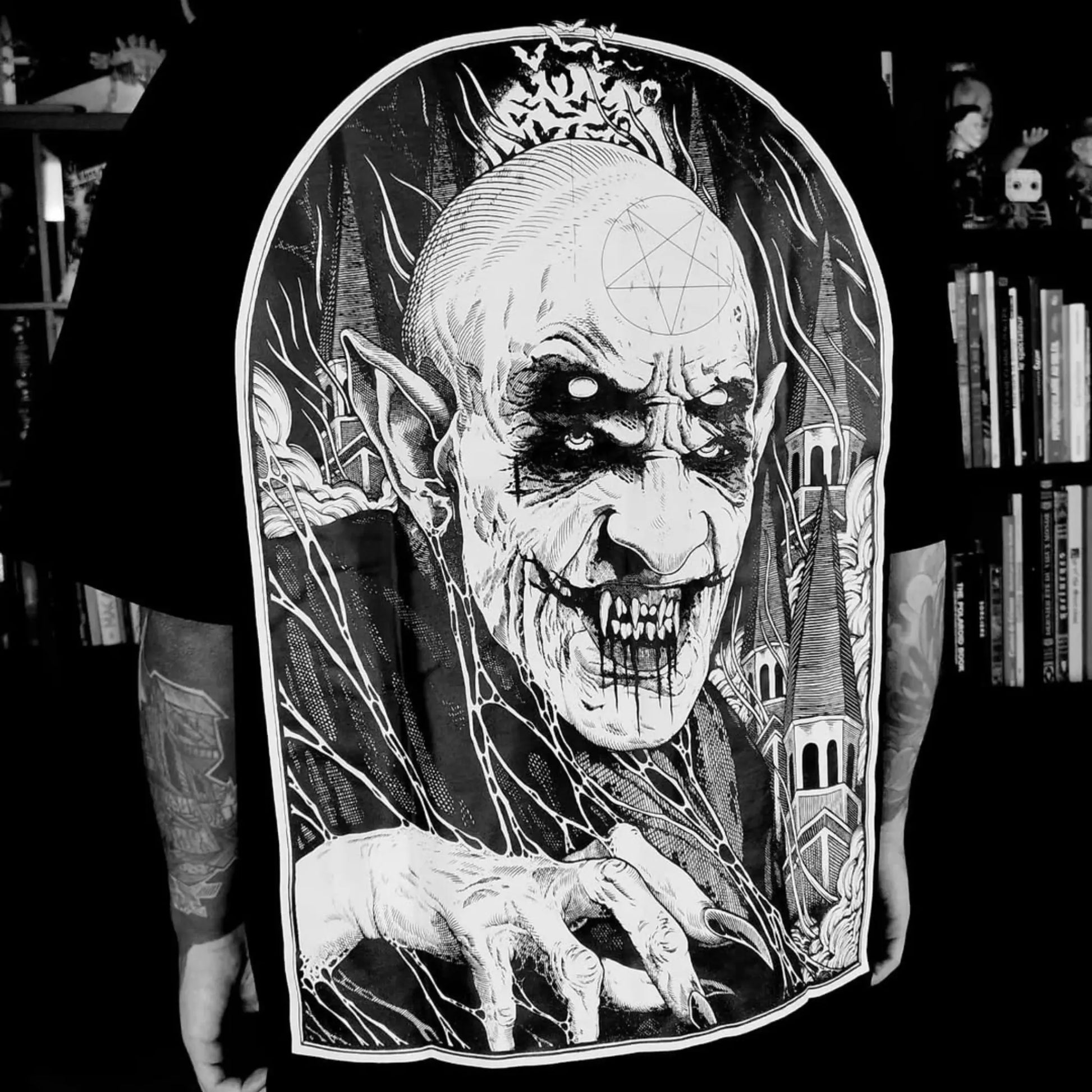 A detailed black and white illustration of an Vampire figure against a bookshelf background. RTLA Apparel